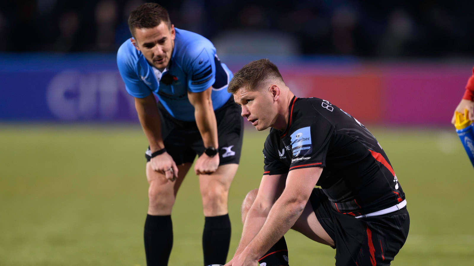 Referee Luke Pearce watching Saracens fly-half Owen Farrell line up a kick.