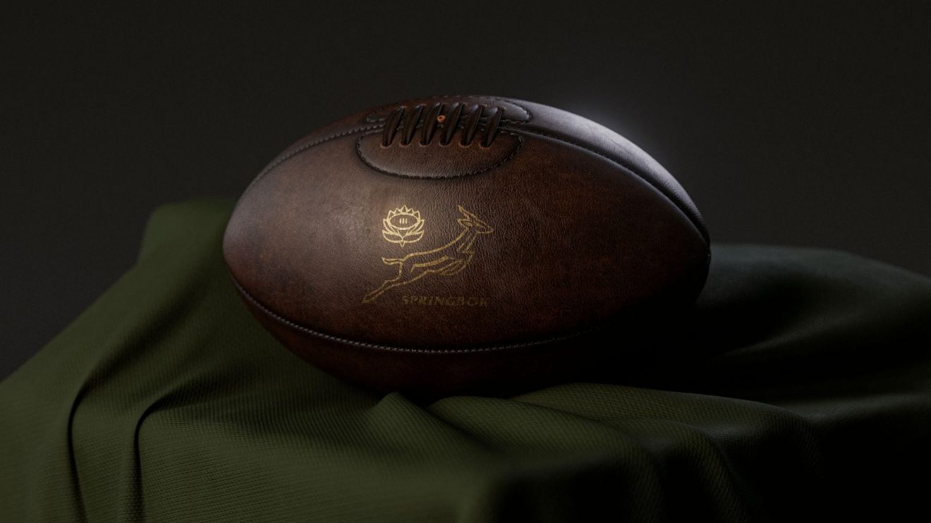 A 3D render of a vintage leather rugby ball with a gold South African rugby logo resting on a draped cloth.